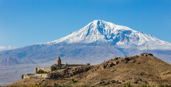 The stone walls of Khor Virap monastery on a low hill, with the snow-covered cone of Mount Ararat rising behind