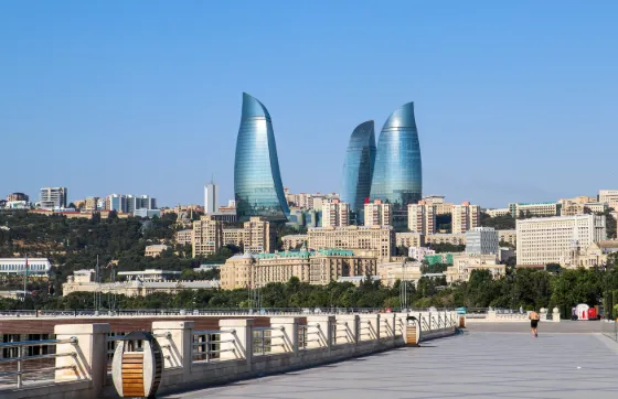The curved glass Flame Towers rising above the low rooftops of Baku, seen from the seafront boulevard