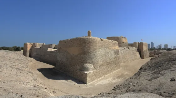 Excavated pale stone walls and ramparts of the fort at Qal'at al-Bahrain, with the city skyline faint behind