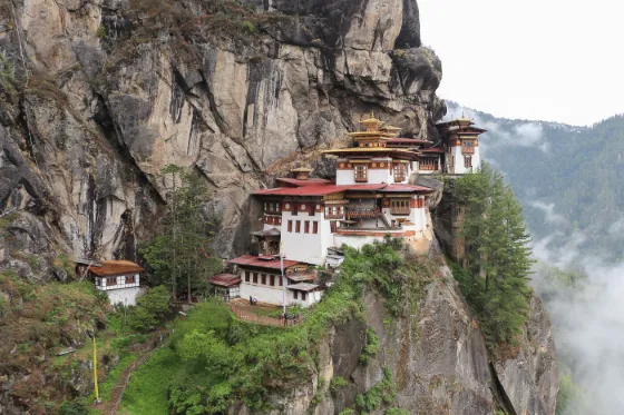 The white-walled Taktsang monastery clinging to a sheer cliff face above a forested valley in Bhutan