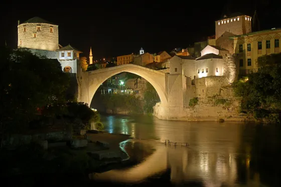 The single stone arch of the rebuilt Ottoman bridge at Mostar lit at night and reflected in the Neretva below