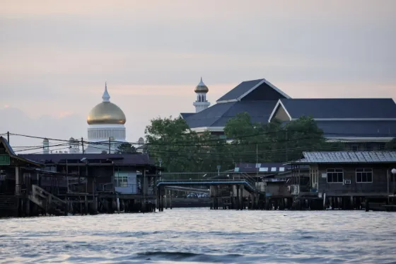 Wooden houses on stilts above the water at Kampong Ayer, with a mosque dome rising behind them