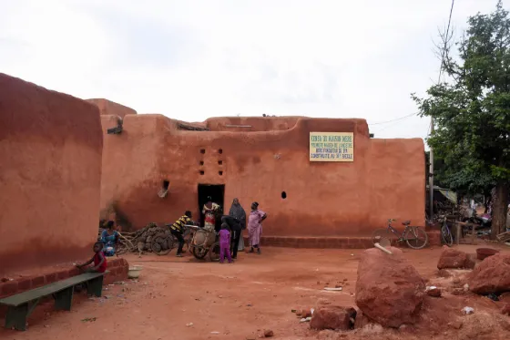 A red earthen building with people sitting in the shade of its doorway, Bobo-Dioulasso, Burkina Faso