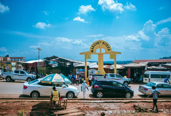 Cars and people at the yellow market gateway on a street in Gitega, Burundi, under a bright sky
