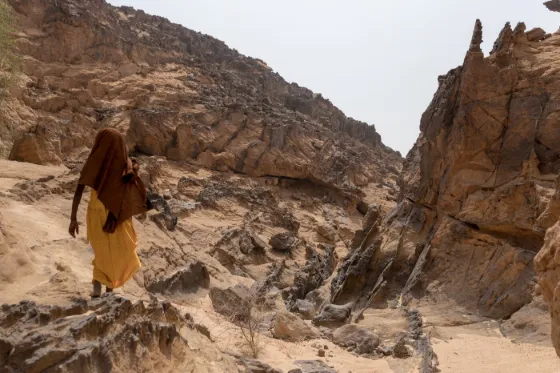 A person in an orange robe walking between weathered sandstone pinnacles on the Ennedi Plateau, Chad