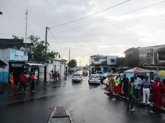 People and parked cars along a wet street of low shops in Moroni, the capital of the Comoros, after rain