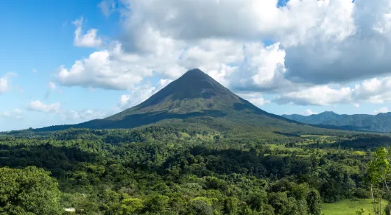 The symmetrical green cone of Arenal Volcano rising from forest under broken cloud, Costa Rica