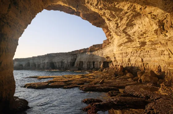 A wide rock arch standing over clear shallow sea at the sea caves of Cape Greco, Cyprus