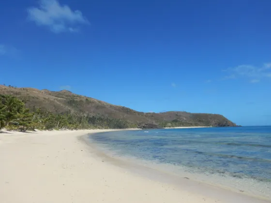 A curve of white sand meeting clear turquoise water below dry green hills on Naviti island, Fiji