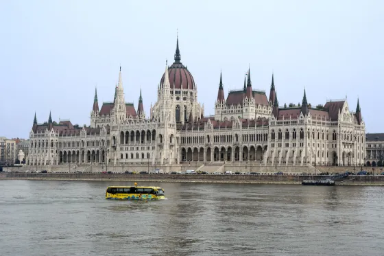 The long neo-Gothic facade and dome of the Hungarian Parliament rising above the Danube in Budapest, with a tour boat passing