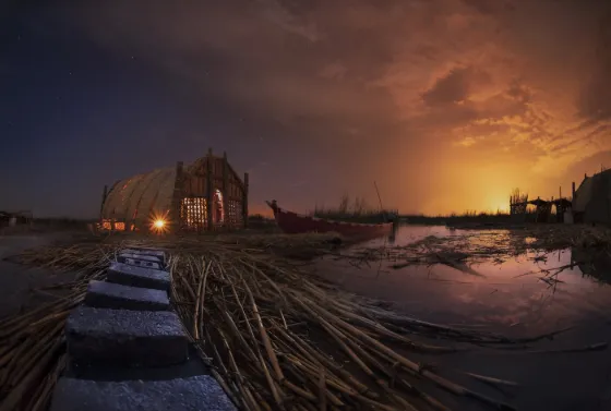 A reed house and narrow boats at the water's edge in the Mesopotamian Marshes of southern Iraq at sunset