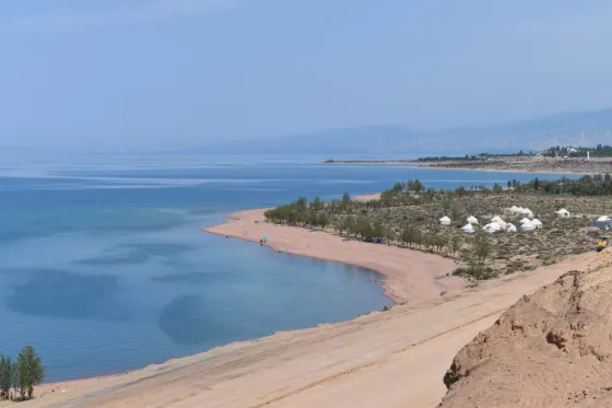 The pale shore of Lake Issyk-Kul curving away below dry mountains, Kyrgyzstan