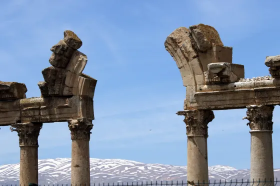 Weathered Roman columns and carved capitals standing at Baalbek, Lebanon, with snow on the mountains beyond