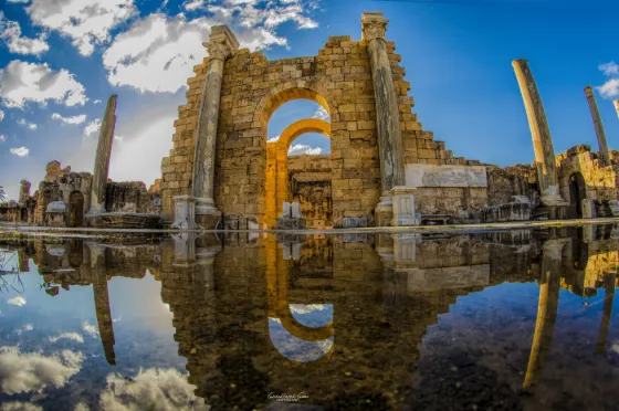 A Roman arch and fallen columns of Leptis Magna lit gold and reflected in standing water, Libya