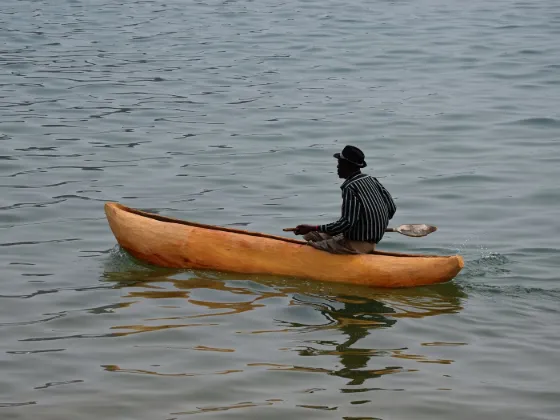 A man paddling a wooden dugout canoe on the calm open water of Lake Malawi