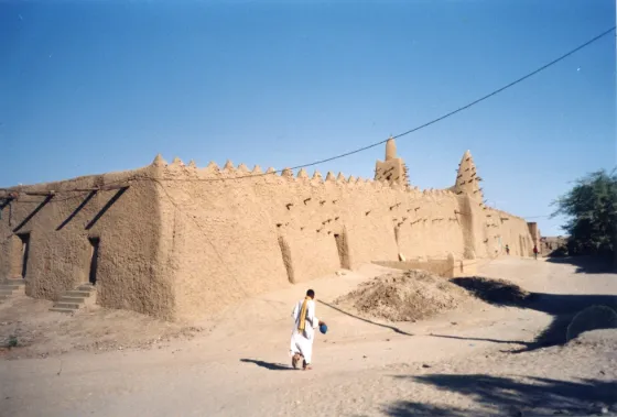 A mud-brick mosque in Timbuktu, Mali, its buttressed walls studded with projecting wooden beams, under a deep blue sky