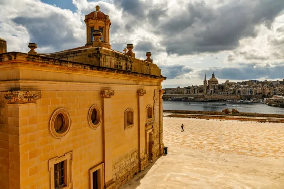 The honey-coloured stone walls of Fort Manoel in Malta, with Valletta's skyline across the harbour
