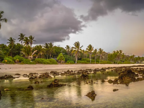 Coral pools and palms on the Nauru coast at dusk, with a faint rainbow over the Pacific