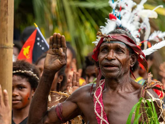 A village elder in traditional dress salutes at a ceremony in Papua New Guinea, the national flag flying behind