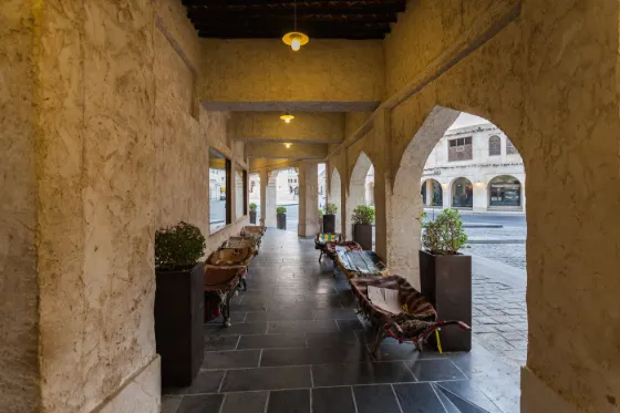A shaded arcade of warm stone arches and wooden benches in Souq Waqif, Doha