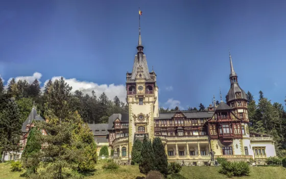 The turrets and timbered gables of Peles Castle set among trees below the Carpathian mountains, Romania