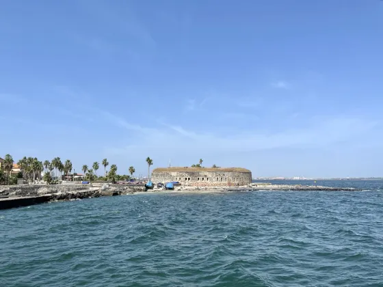 Low colonial buildings along the rocky shore of Goree Island, with the Atlantic in the foreground