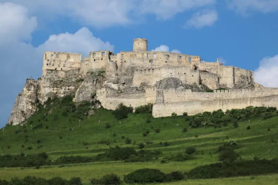 The pale ruined walls and keep of Spis Castle spread along a green hilltop, Slovakia