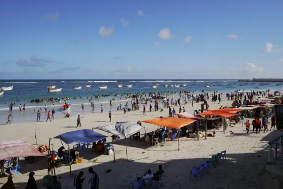 Crowds, parasols and small boats along Lido Beach in Mogadishu, with the city's buildings behind