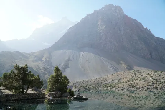 The still blue water of Iskanderkul below the steep grey ridges of the Fann Mountains, Tajikistan