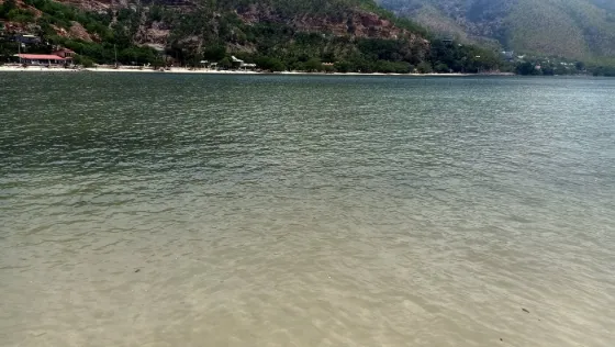 Calm shallow water along the shore of Atauro island, with green hills and scattered roofs behind